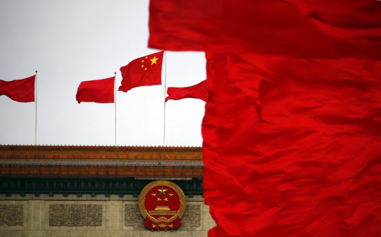 Red flags flutter next to a national emblem and a national flag of China on top of the Great Hall of the People, which is the venue of the closing ceremony of the Chinese People’s Political Consultative Conference (CPPCC), in Beijing, March 12, 2014. REUTERS/Petar Kujundzic (CHINA – Tags: POLITICS) – RTR3GOJ6